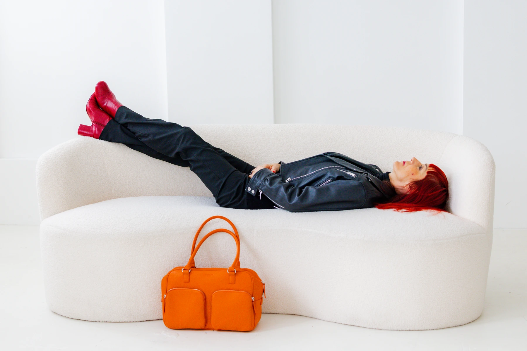 Rothaarige Unternehmerin auf einem cremefarbenen Sofa mit einer orangefarbenen Tasche