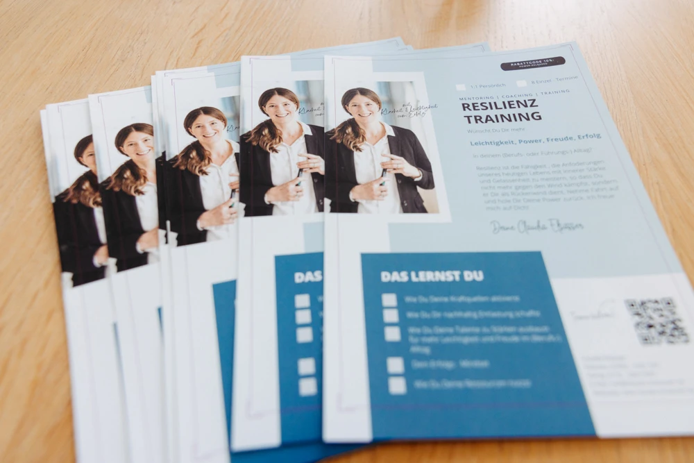 Flyer für ein Resilienztraining liegt auf einem Holztisch. Fotografin: Manuela Engelking. Aufnahmeort: Frankfurt.