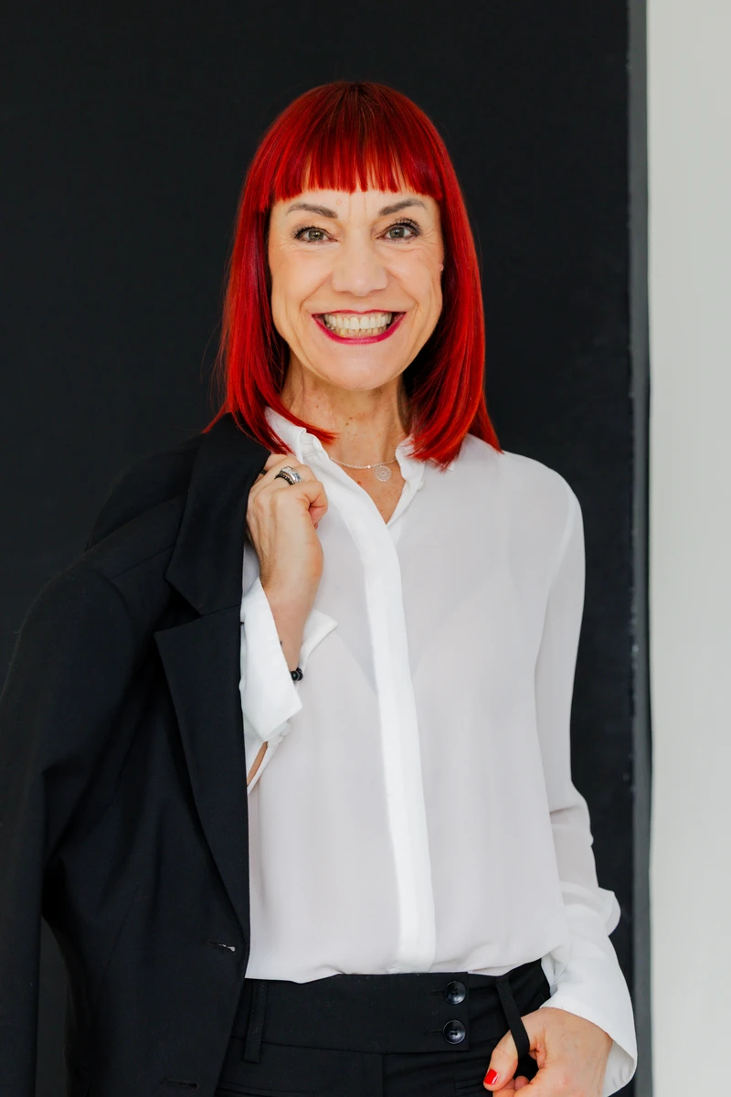 Unternehmerin mit rotem Haar lächelt in weißer Bluse. Fotografin: Manuela Engelking. Aufnahmeort: Lüneburg.
