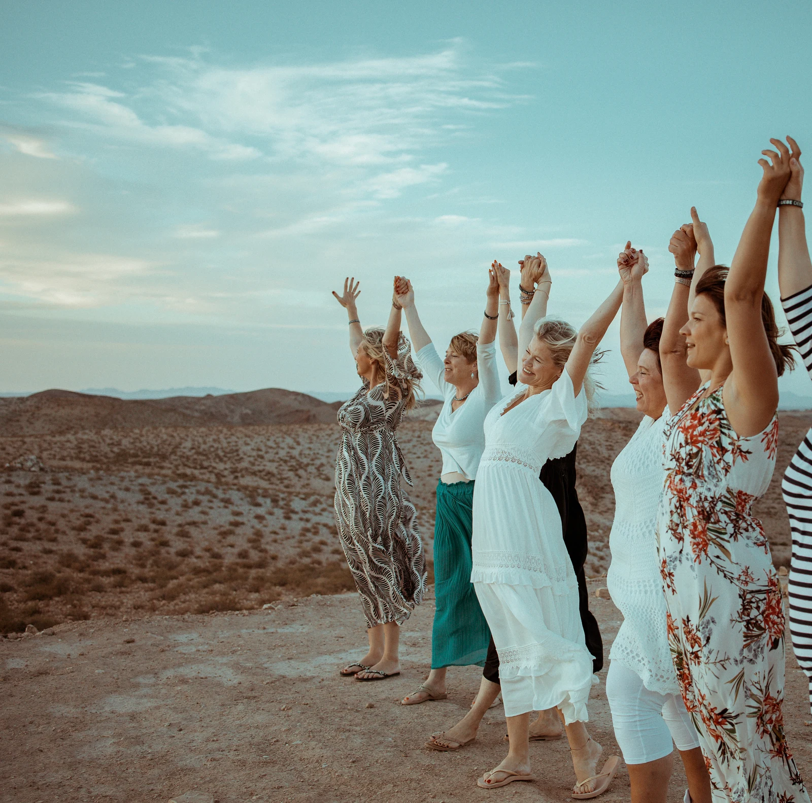 Frauengruppe beim Retreat in Marrakesch Frauen stehen mit erhobenen Armen nebeneinander in einer Wüstenlandschaft