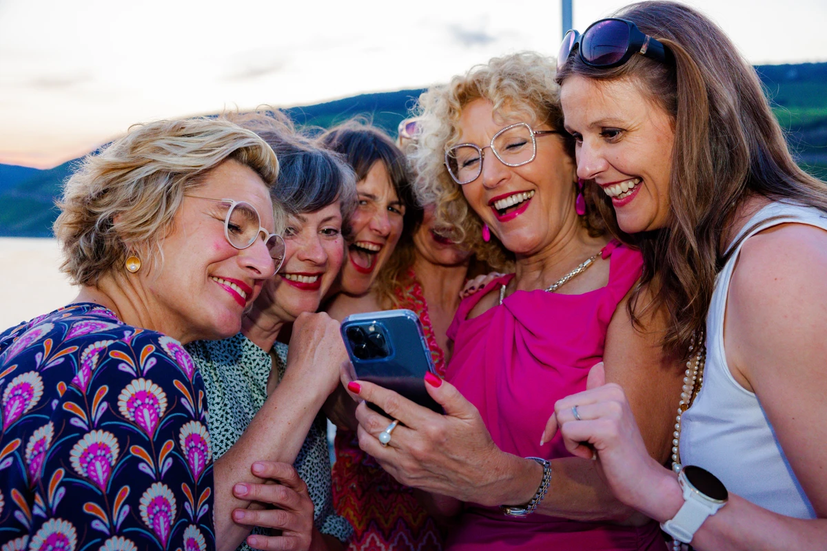 Frauen lachen beim gemeinsamen Blick auf ein Smartphone im Freien