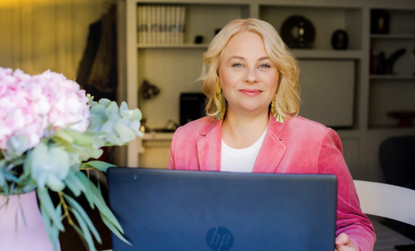 Unternehmerin am Laptop VIP Shooting-Tag in Hamburg: Blonde Unternehmerin im rosa Blazer blickt hinter ihrem Laptop in die Kamera; Blumen vorn.