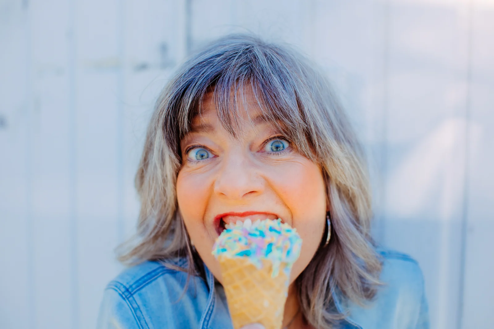 Portrait mit Eiswaffel VIP Shooting-Tag in Norwegen: Grauhaarige Unternehmerin lacht mit einer bunten Eiswaffel vor hellblauer Wand.