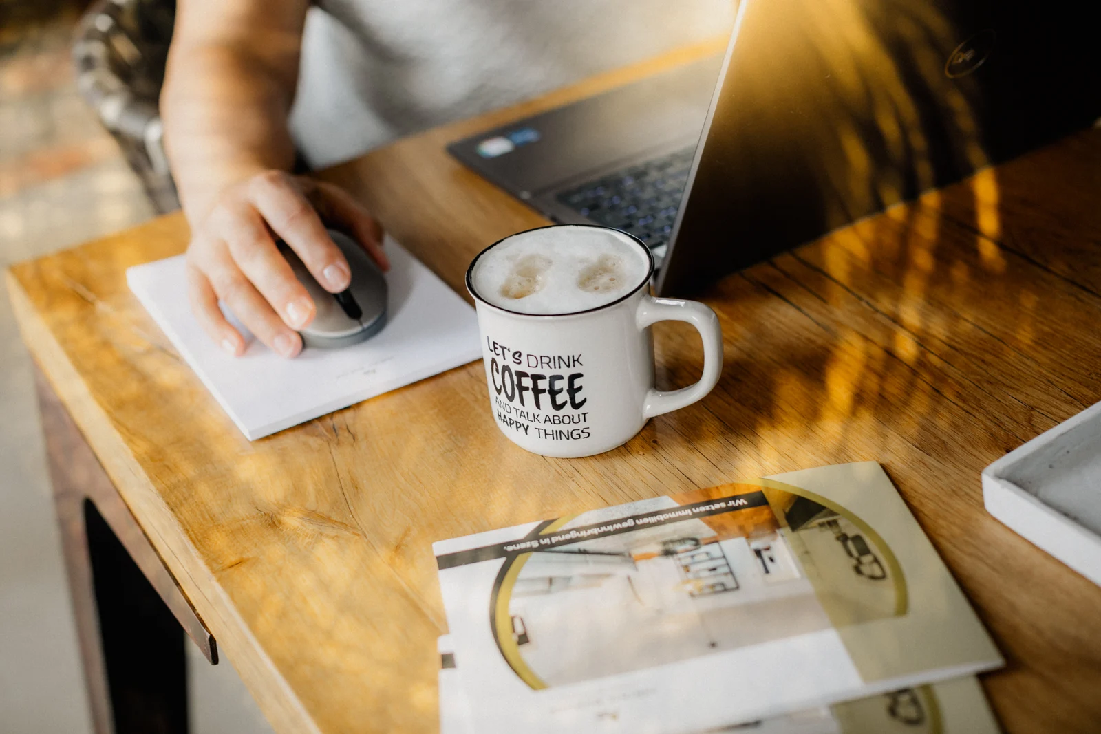 VIP Shooting-Tag in Solingen: Eine Hand liegt auf der Computermaus neben einer Kaffeetasse und einem Laptop auf Holztisch.