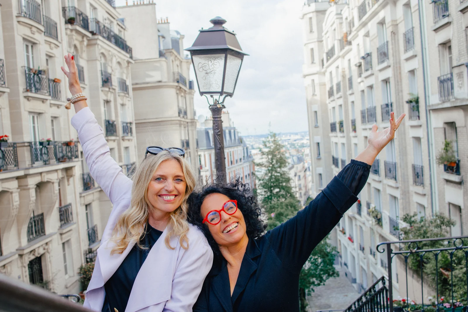 Susanne Pillokat-Tangen und Nicole Frenken lächeln mit erhobenen Armen auf einer Treppe in Paris.